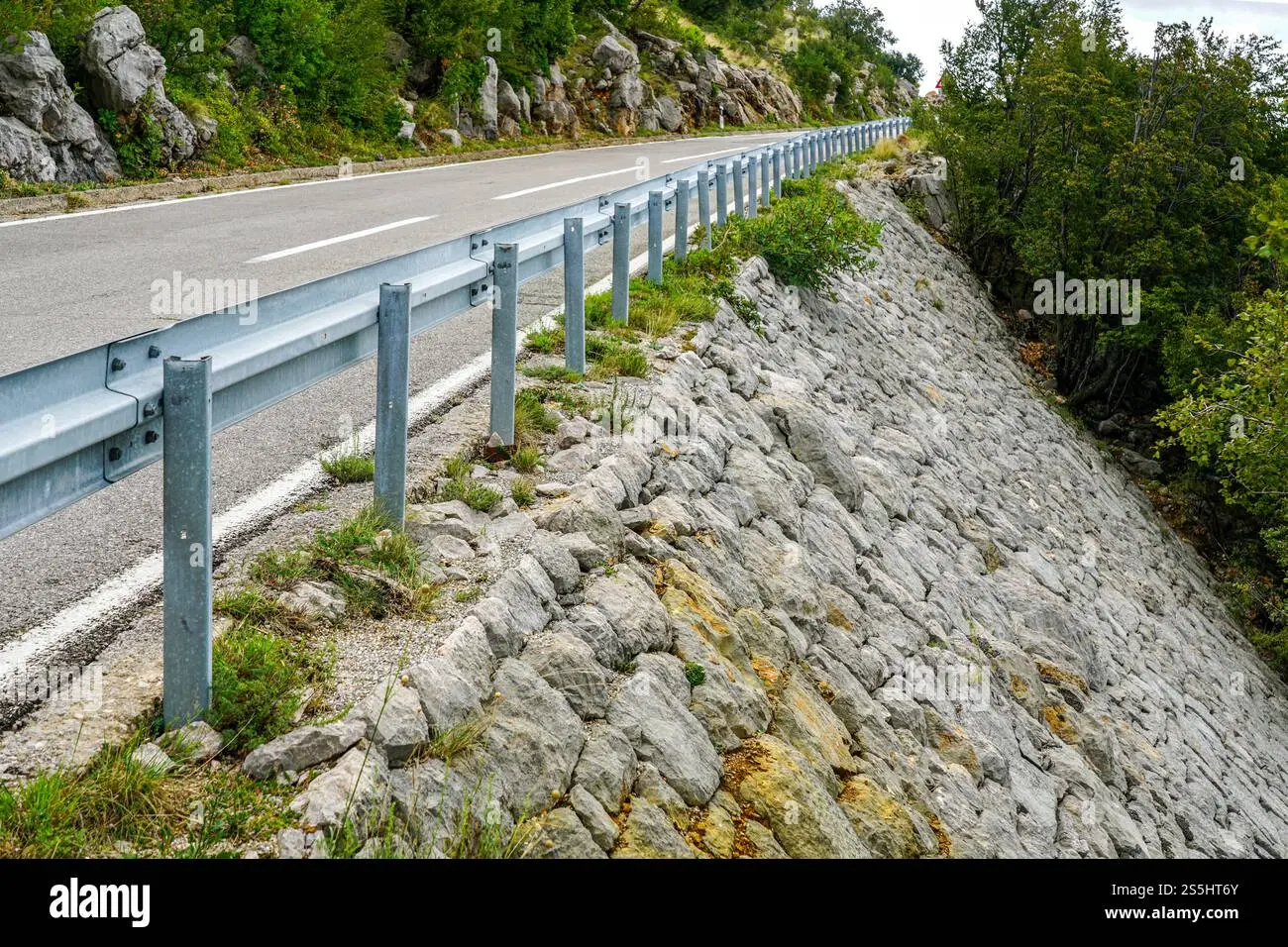 شیب تند راه با سنگ‌های بزرگ پوشیده شده و محصور شده توسط مانع فلزی برای افزایش ایمنی ترافیکی